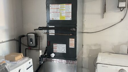 Vertical HVAC air handler installed inside a utility closet with new condensate drain and refrigerant lines