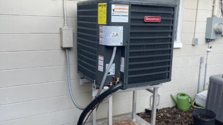 Side view of a residential outdoor AC condenser installed on a raised platform for improved flood protection and airflow