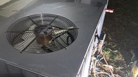 HVAC technician performing nighttime air conditioner service with refrigerant gauges connected to the outdoor condenser